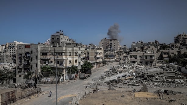 The ruins of dozens of buildings in Gaza can be seen with smoke rising against a blue sky
