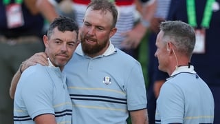 Shane Lowry of Team Europe hugs teammate Rory McIlroy as they talk to Captain Luke Donald of Team Europe after they tied their match with Patrick Cantlay and Sam Burns of Team United States during the Friday afternoon four-ball matches of the 2025 Ryder C