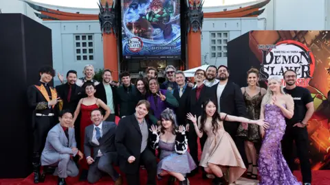 Getty Images A group of people dressed in suits and gowns gather outside a cinema on a red carpet, flanked by posters for Demon Slayer, Kimetsu no Yaiba Infinity Castle. The mood is celebratory.