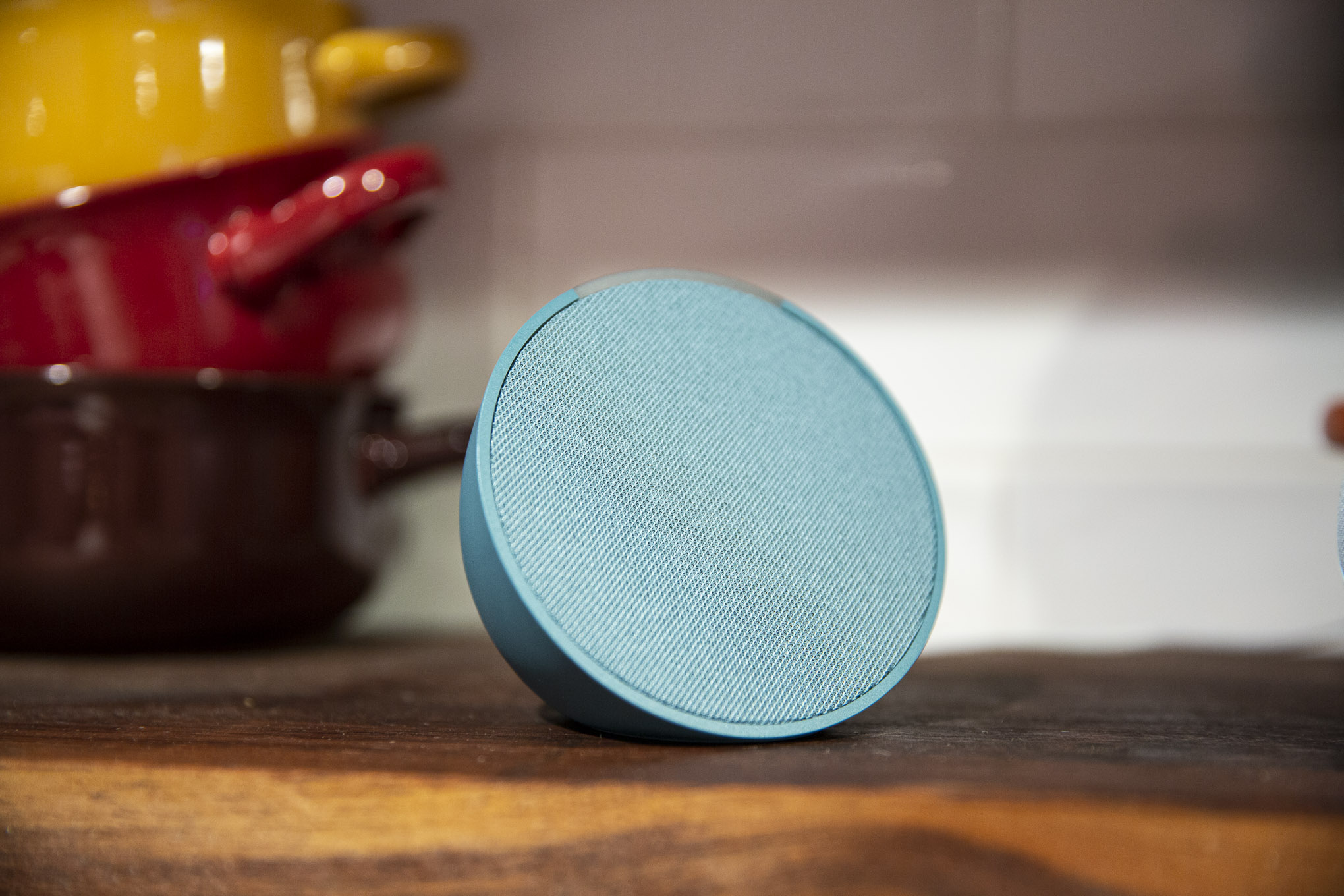 Teal Amazon Echo Pop viewed at an angle with colorful pots in the background.