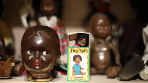 EPA A shelf with black dolls of different types and sizes in Rene Matic's installation