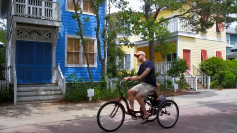 Getty Images Man on bike going past colourful buildings in town of Seaside, Florida