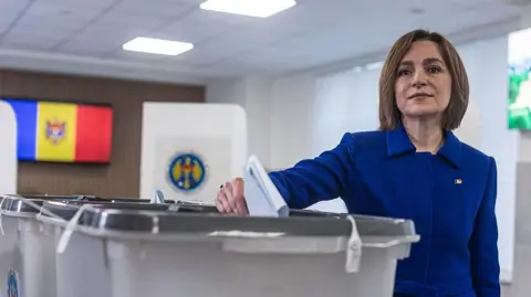 Anadolu via Getty Images Moldova's president dressed in a blue suit and with brunette hair poses for the cameras as she casts a ballot
