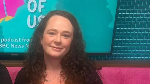 Louise McCullough. She has long dark curly hair, sitting on a pink sofa with the State of Us branding on a screen behind her.
