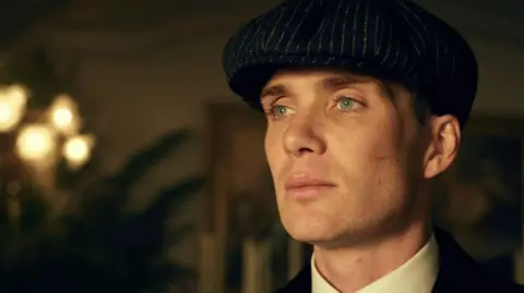 BBC Studios Cillian Murphy in character as Thomas Shelby wearing a cap and white shirt