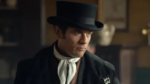 Netflix James Norton in character as Sean Rafferty wearing a black top hat and white scarf