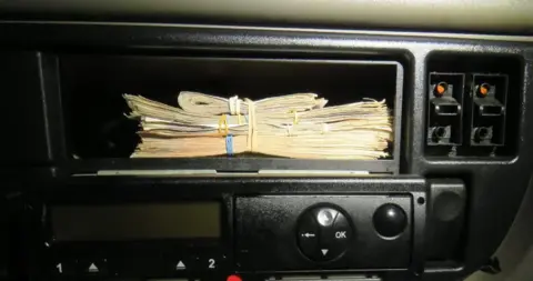 National Crime Agency A photo of a stack of bank notes in a panel above a radio, seized during the people smuggling operation allegedly linked to Goran Jalal.